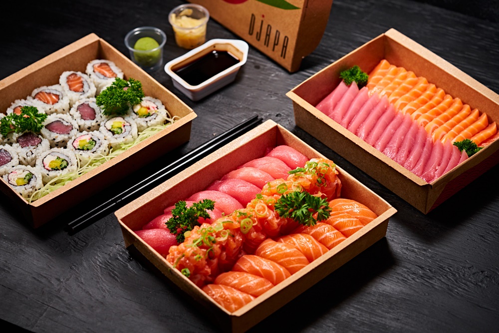 porções de uramaki de sabores variados, sashimis de atum e salmão e niguiris em caixas de papelão para delivery