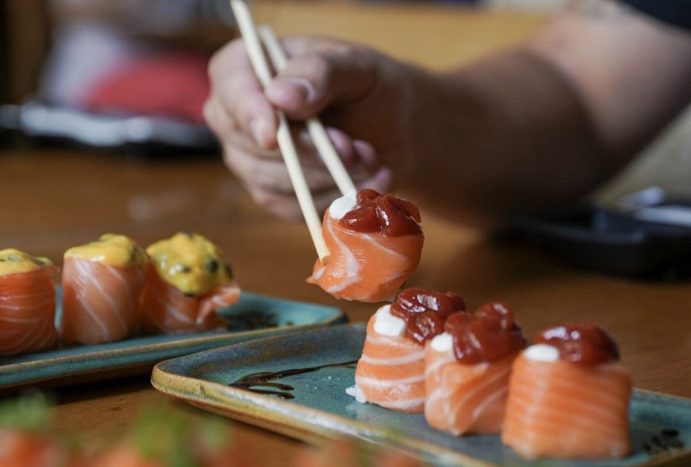 mão de uma pessoa pegando um sushi usando o hashi